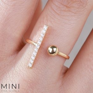 May include: Gold ring with a vertical bar set with clear cubic zirconia stones and a round ball on the opposite side.