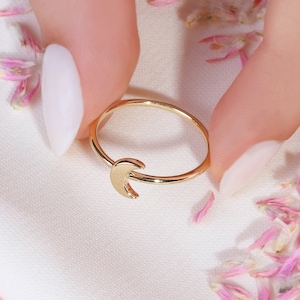 May include: A gold crescent moon ring on a white background with pink flower petals.