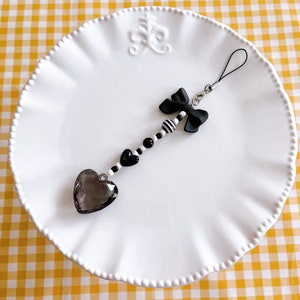 May include: A black and white beaded phone charm with a black bow and a clear heart-shaped crystal.