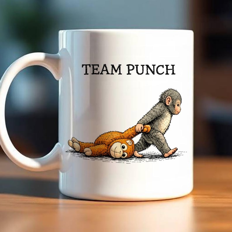 May include: White ceramic mug with the text "TEAM PUNCH" and a cartoon illustration of a gray monkey pulling a brown monkey. The mug has a large, curved handle.