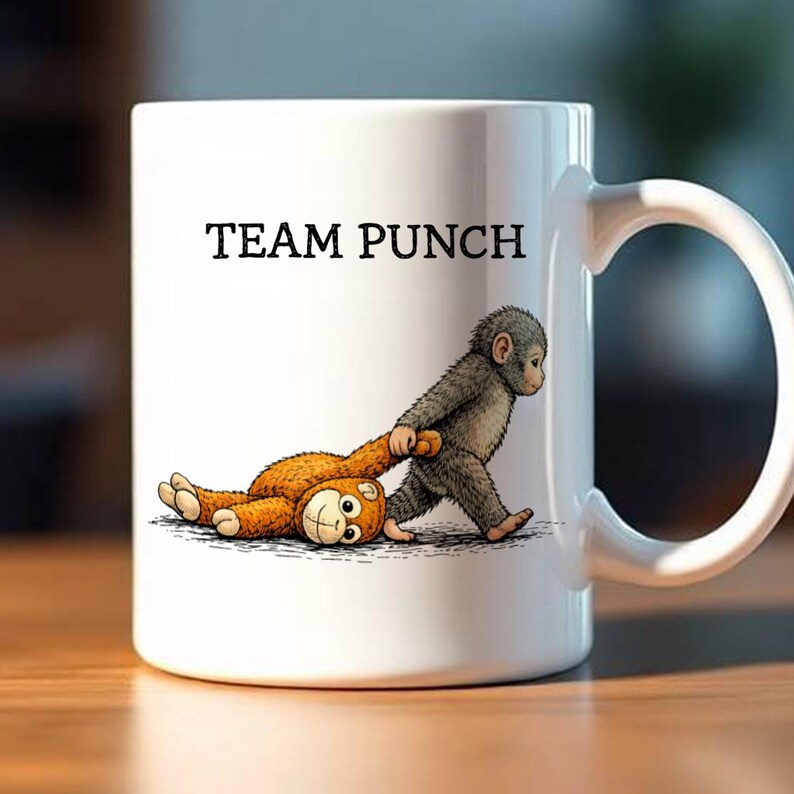 May include: White ceramic mug with the text "TEAM PUNCH" in black. The mug features a cartoon illustration of a gray monkey pulling a brown teddy bear. The teddy bear is lying on its back with a smiling face.