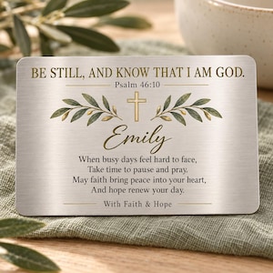 May include: A rectangular silver-toned metal wallet card featuring the text BE STILL, AND KNOW THAT I AM GOD. Psalm 46:10, a gold cross icon, olive branches, the name Emily, and a poem ending with the phrase With Faith & Hope.