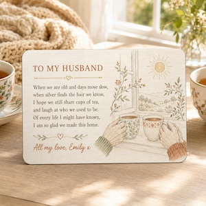 May include: A rectangular wooden plaque featuring the text TO MY HUSBAND followed by a poem about aging and sharing tea. The design includes an illustration of two hands holding mugs by a window with a sun and landscape view, signed All my love, Emily x.