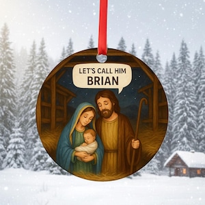 Op de afbeelding: Ronde kerstversiering met een kerststal met Maria, Jozef en het kindje Jezus. De versiering heeft een rood lint om op te hangen en de tekst "LET'S CALL HIM BRIAN" in een tekstballon. De achtergrond toont een besneeuwd landschap.