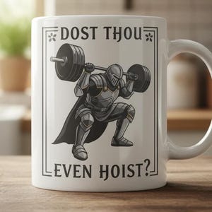 Może przedstawiać: Biały ceramiczny kubek z czarno-szarą ilustracją rycerza podnoszącego sztangę. Kubek ma czarny napis "DOST THOU EVEN HOIST?" w czarnym kolorze, obramowany ozdobną obw&oacute;dką. Kubek ma biały uchwyt.