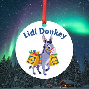 May include: A circular Christmas decoration with a cartoon donkey carrying shopping bags branded with the Lidl logo. The words "Lidl Donkey" are above the donkey. The ornament has a red ribbon for hanging, set against a winter forest scene with the Northern Lights.