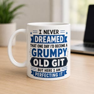 Puede incluir: Una taza de cerámica blanca con texto en azul y azul oscuro que dice: I NEVER DREAMED THAT ONE DAY I'D BECOME A GRUMPY OLD GIT BUT HERE I AM PERFECTING IT. El diseño incluye líneas decorativas y estrellas que rodean la tipografía.