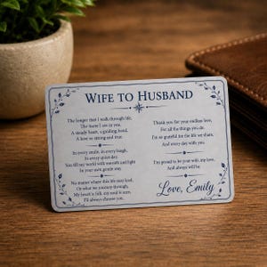May include: A rectangular silver-toned metal wallet card featuring the blue printed text WIFE TO HUSBAND, a sentimental poem, and the signature Love, Emily. The card is decorated with delicate blue floral vine borders and small star icons.