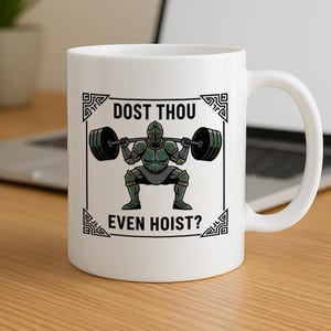 Pode incluir: Caneca de cerâmica branca com um desenho de um cavaleiro levantando pesos. O cavaleiro, com armadura verde e cinza, levanta uma barra. A caneca tem o texto "DOST THOU EVEN HOIST?" em preto, emoldurado por elementos decorativos.