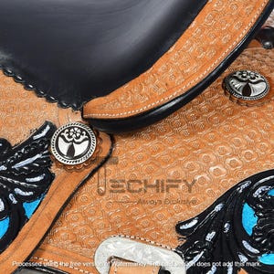 May include: Close-up of a western saddle with intricate tooling and decorative silver conchos. The saddle features black leather accents, turquoise details, and a floral pattern embossed on the tan leather. The saddle is a detailed piece of equestrian equipment.