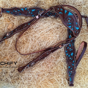 May include: A brown leather horse bridle with turquoise floral embroidery and silver accents. The bridle is laid out on a bed of brown packing peanuts.