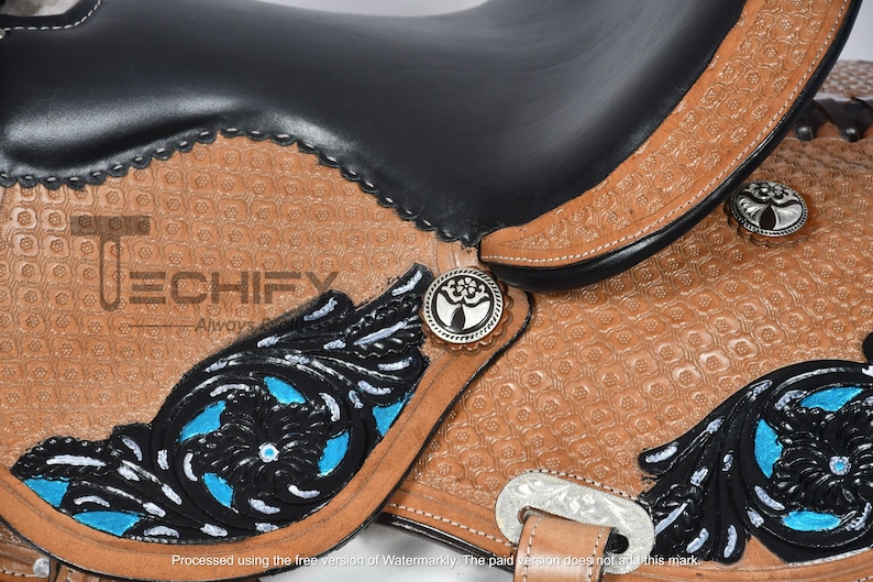 May include: Close-up of a Western saddle with a black seat and brown leather detailing. The saddle features intricate floral designs in black and turquoise, with silver-toned conchos and hardware. The leather has a textured pattern.