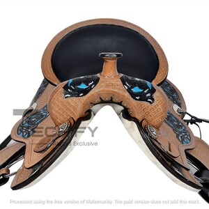 May include: A brown and black Western saddle with intricate tooling and turquoise accents. The saddle features a black seat and decorative silver-toned studs. The stirrups and other hardware are visible.