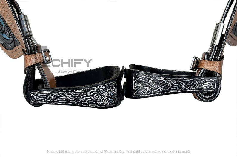 May include: Pair of black and silver Western stirrups with intricate floral designs. The stirrups have a black interior and are accented with silver detailing. Brown leather straps and metal hardware complete the design. The word "CHIFY" is visible.