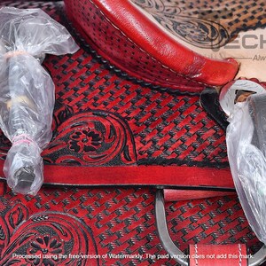 May include: Close-up of a red leather saddle with black floral embroidery and a woven pattern. The saddle is covered in clear plastic wrap.