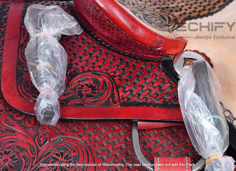 May include: Close-up of a red leather saddle with black floral embroidery and a woven pattern. The saddle is covered in clear plastic wrap.