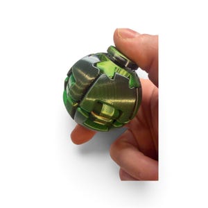 May include: A spherical fidget toy with a metallic green finish, featuring interlocking geometric segments and a smooth, rounded surface. The object has a complex, layered construction with visible seams between the individual green components.