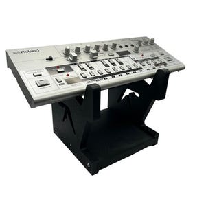 May include: A silver Roland synthesizer sits on a black wooden stand. The synthesizer has numerous knobs, buttons, and keys. The stand is made of black wood and has a geometric design.