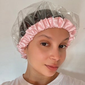 Puede incluir: Un gorro de ducha de plástico transparente con forro de satén rosa. El gorro está diseñado para proteger el cabello del agua.