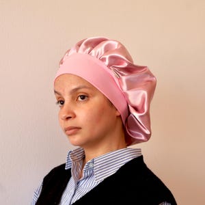 Puede incluir: Un gorro de dormir de satén rosa con una banda elástica ancha. El gorro está diseñado para proteger el cabello mientras se duerme.