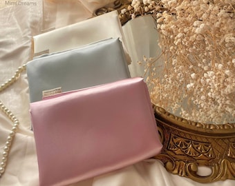 Pode incluir: Três peças de tecido em cores diferentes: marfim, azul claro e rosa. O tecido é suave e sedoso. O tecido está dobrado e empilhado um em cima do outro. O tecido está sobre uma superfície branca.