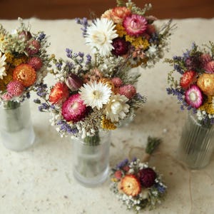 Colorful dried wildflower table arrangements in glass bud vases. A mix of naturally dried strawflowers, gomphrena, wild grasses, ammobium and baby's breath. Custom floral table decor for all occasions.