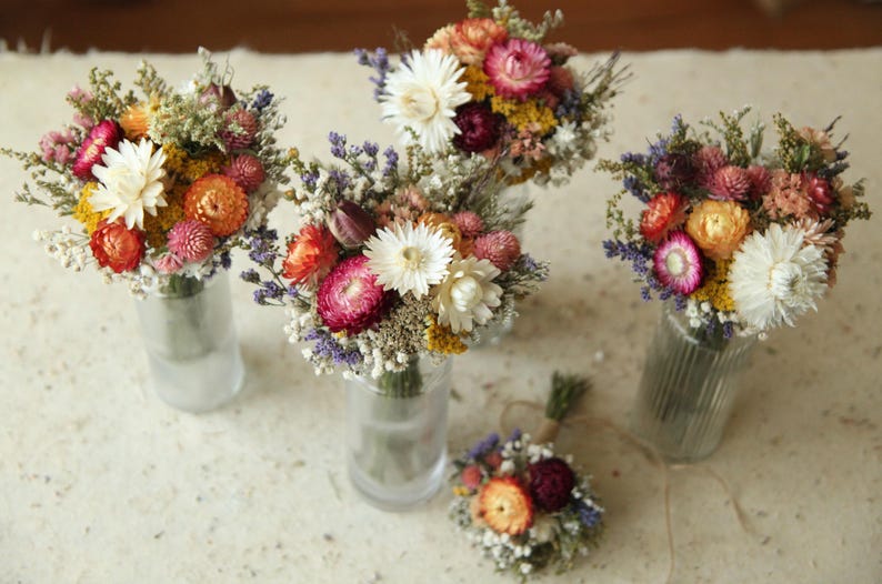 Colorful dried wildflower table arrangements in glass bud vases. A mix of naturally dried strawflowers, gomphrena, wild grasses, ammobium and baby's breath. Custom floral table decor for all occasions.