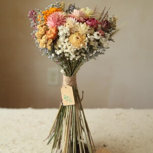 This photo features variation I of the listing, with a bright pastel mix of creamy and blush strawflowers, marigolds and daisies with mixed wildflowers and wild grasses. The size is a small, perfect as a floral gift, bridesmaid and elopement bouquet. Wildflower Wedding cottage garden home decor.