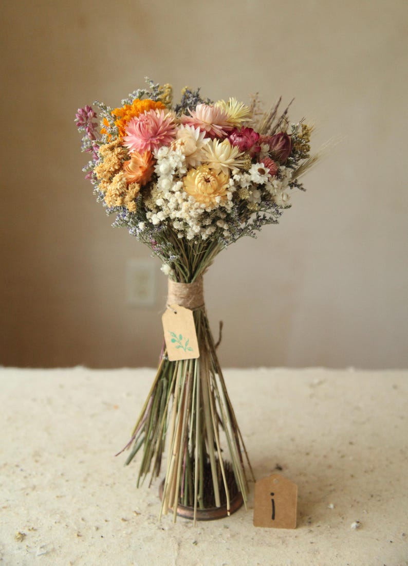 This photo features variation I of the listing, with a bright pastel mix of creamy and blush strawflowers, marigolds and daisies with mixed wildflowers and wild grasses. The size is a small, perfect as a floral gift, bridesmaid and elopement bouquet. Wildflower Wedding cottage garden home decor.