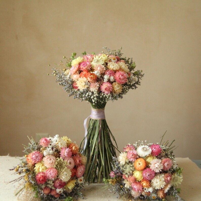 Custom XL Bridal Bouquet with two medium dried flower bridesmaid bouquet laying on each side. Bright pastel tones of creamy white, blush, pink, yellow and peach.