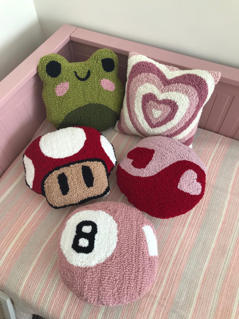 Puede incluir: Cinco almohadas decorativas de colores y cosidas a mano con diferentes dise&ntilde;os. Las almohadas est&aacute;n hechas de una tela suave y mullida y presentan una rana verde, un hongo rojo, un coraz&oacute;n rosa, un s&iacute;mbolo yin-yang rojo y rosa y una bola de billar rosa.