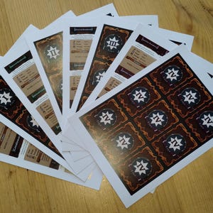 May include: A collection of printed game cards fanned out on a wooden surface. The cards feature a brown and white design with star-like symbols and text. Some cards have a dark green border.