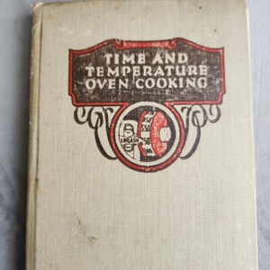 May include: A vintage off-white hardcover book titled Time and Temperature Oven Cooking. The cover features a black and red graphic illustration of a circular oven thermometer dial with the text clearly printed in a decorative rectangular frame.