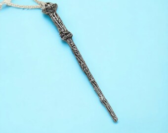 May include: A silver wand with a detailed design, hanging from a white string on a light blue background.