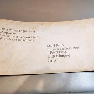 May include: A vintage-looking envelope addressed to Mr. H. Potter, The Cupboard under the Stairs, 4 Privet Drive, Little Whinging, Surrey. The return address is Albus Percival Wulfric Brian Dumbledore, Headmaster of Hogwarts School of Witchcraft and Wizardry.