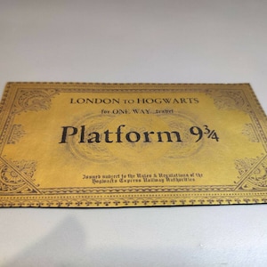 May include: A gold ticket with a black border and ornate design. The ticket reads "LONDON TO HOGWARTS for ONE WAY travel Platform 9 3/4" and "Issued subject to the Rules & Regulations of the Hogwarts Express Railway Authorities".