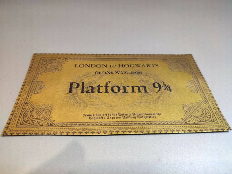 May include: A gold ticket with a black border and ornate design. The ticket reads "LONDON TO HOGWARTS for ONE WAY travel Platform 9 3/4" and "Issued subject to the Rules & Regulations of the Hogwarts Express Railway Authorities".