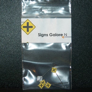 May include: A clear plastic bag with a white label that says "Signs Galore N". Inside the bag are four yellow and black road signs with a cross symbol.
