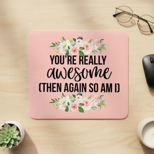May include: A pink mousepad with the text "YOU'RE REALLY awesome (THEN AGAIN SO AM I)" in black script. The mousepad is decorated with floral arrangements in white, pink, and green.