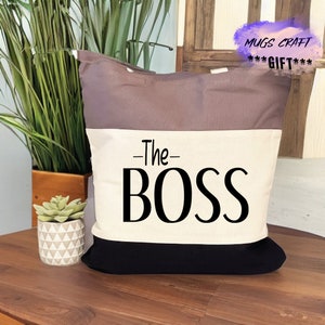 May include: A white canvas tote bag with black trim and a brown top. The bag has the text "The Boss" printed in black on the front.