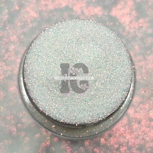 May include: A close-up of a white iridescent glitter in a clear jar with a black label that says "Island Glitter".