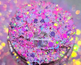 Könnte beinhalten: Ein Glas gefüllt mit einer lebendigen Mischung aus Glitzer in Rosa-, Lila- und schillernden Farbtönen. Die Glitzerstücke variieren in Größe und Form, einschließlich Sechsecken und kleineren Partikeln, wodurch ein strukturiertes, funkelndes Aussehen entsteht. Das Glas ist teilweise sichtbar.