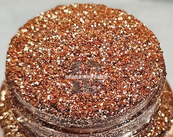 May include: A close-up of a jar of copper glitter with a fine shimmer. The glitter is a mix of copper and gold colors.