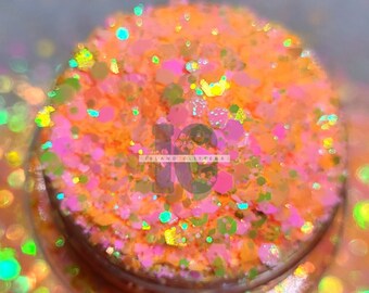 May include: Close-up of a jar of orange, pink, and green glitter. The glitter is iridescent and has a variety of sizes. The jar is labeled "Island Glitters".