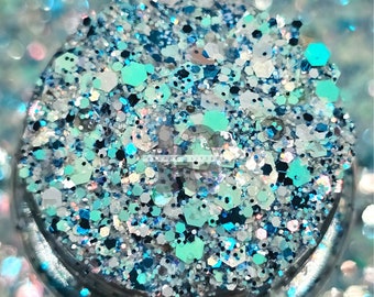May include: A close-up of a jar filled with blue, green, white, and silver glitter. The glitter is a mix of different shapes and sizes.