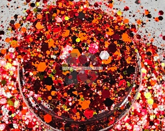 May include: A close-up of a jar filled with red, orange, and black glitter. The glitter is a mix of different shapes and sizes.