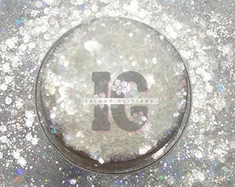 Può includere: Primo piano di glitter bianco con scintillio iridescente. Il glitter è in un contenitore trasparente con il testo "Island Glitters" e le lettere "IG" in un cerchio.