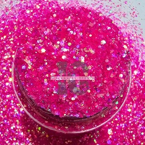 Puede incluir: Primer plano de un tarro lleno de purpurina rosa con brillo iridiscente. La purpurina es una mezcla de tamaños pequeños y grandes.