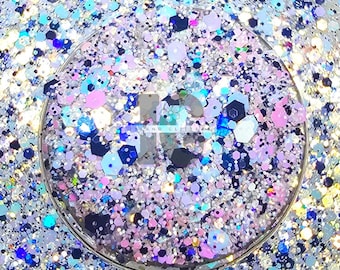May include: A close-up of a container filled with a mix of iridescent glitter. The glitter pieces are in various shapes and sizes, including hexagons and small dots. Colors include silver, blue, pink, and purple.
