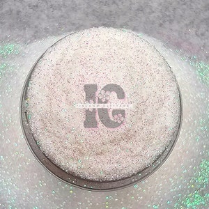 May include: A close-up of a white iridescent glitter in a clear jar. The glitter is very fine and has a subtle shimmer. The jar is labeled "Island Glitter".